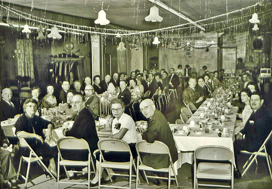 black and white photo of people sitting around tables at a christmas party